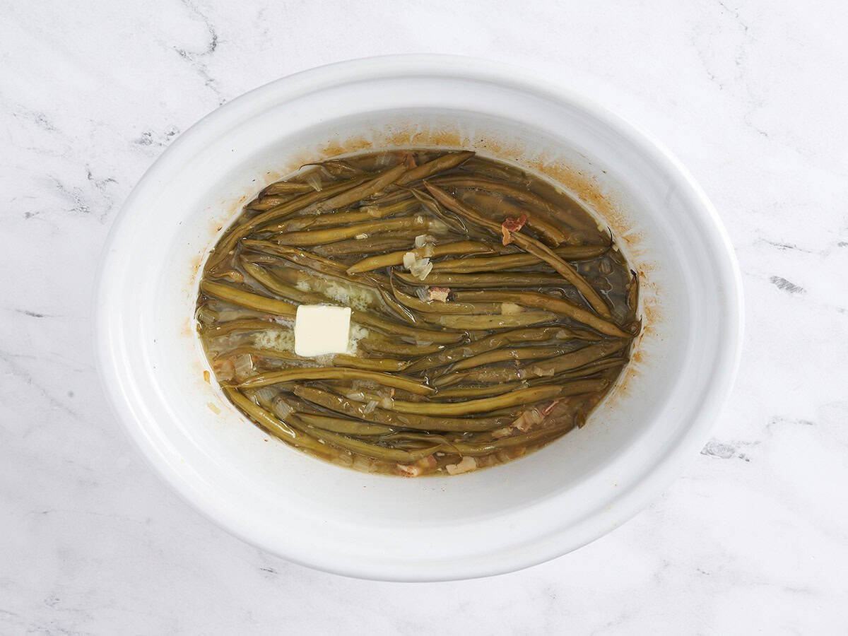 Green beans in a crockpot with a pat of butter.