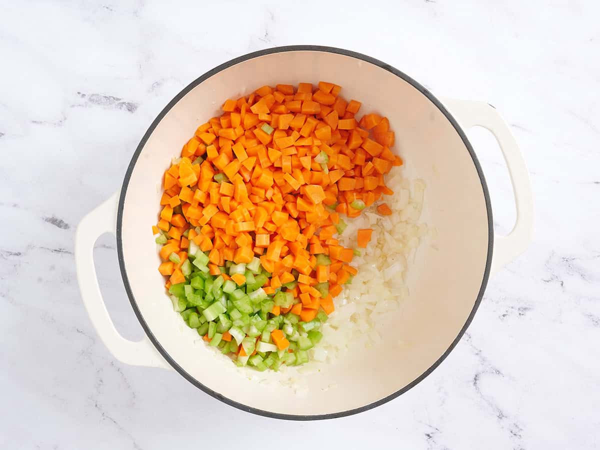Carrots and celery added to onion in a pan.