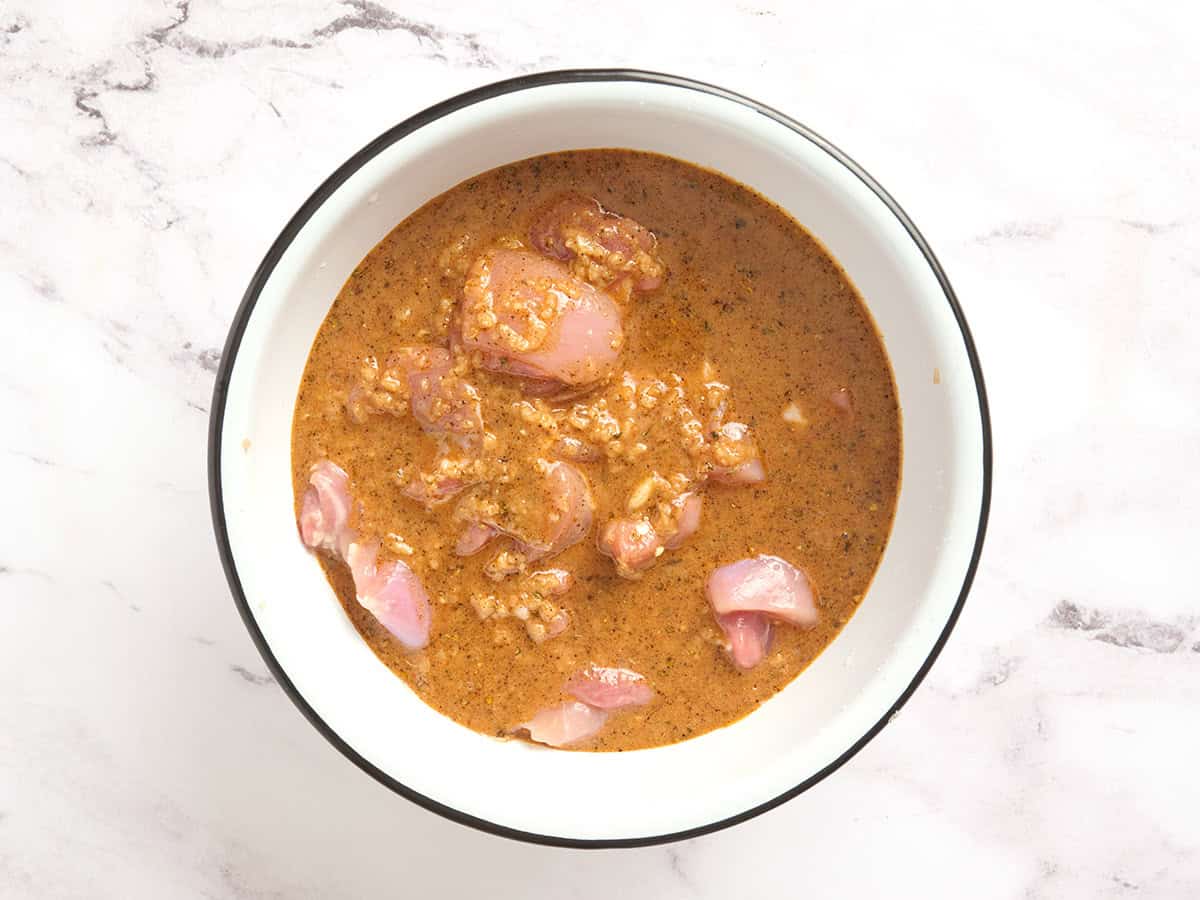 Chicken thigh pieces marinating in a yogurt marinade.