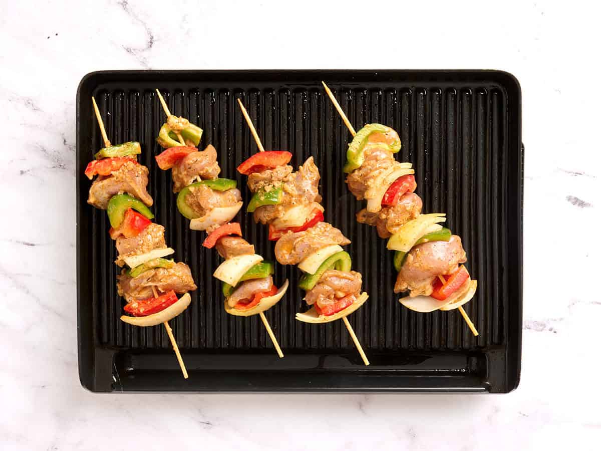 Chicken kabobs cooking on a grill with a meat thermometer checking the internal temperature.
