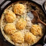 Overhead view of a biscuits and gravy bake in a skillet with a wooden spoon.