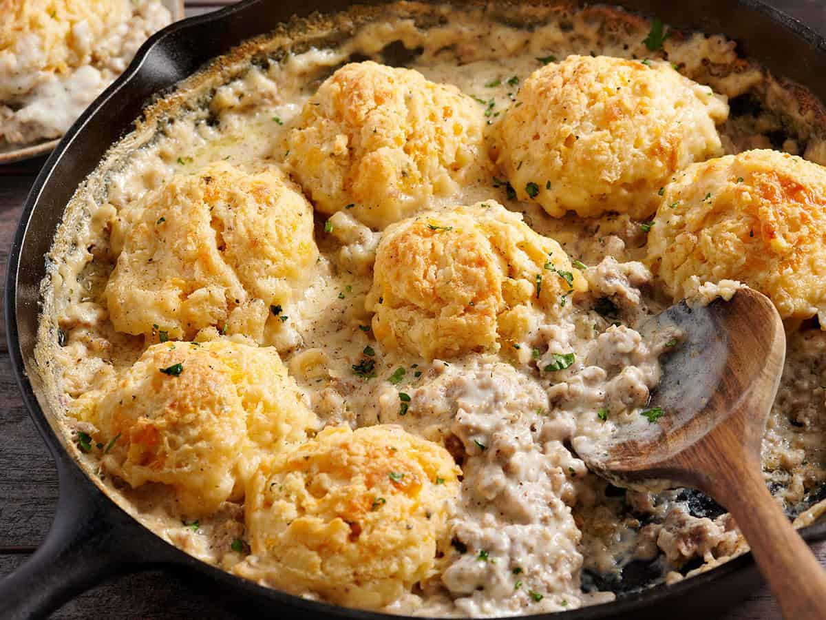 Side view of a biscuit and gravy bake in a skillet with a wooden spoon.