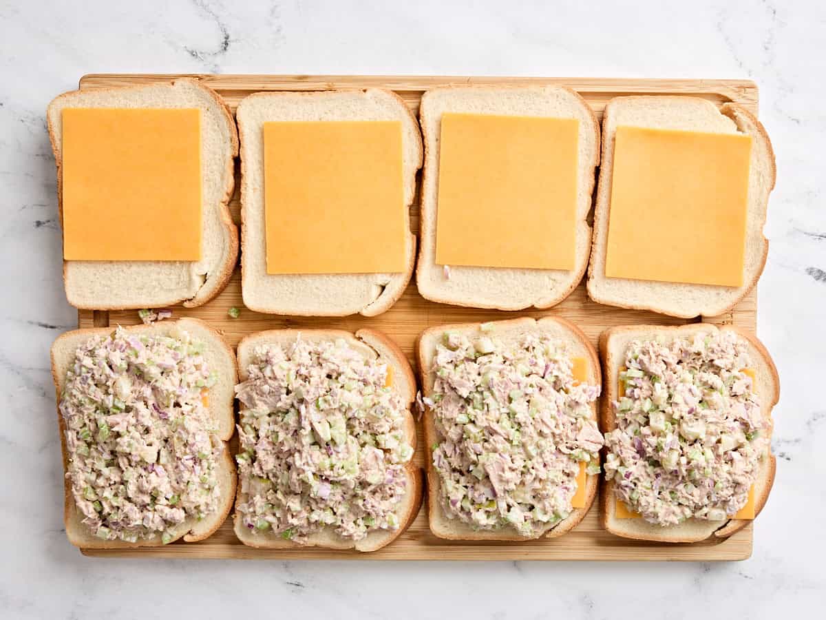 Four slices of bread with a slice of cheese on top and four slices of bread with the tuna mixture on top.