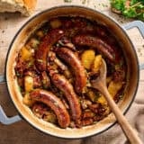 Overhead view of dublin coddle in a dutch oven with a wooden spoon.