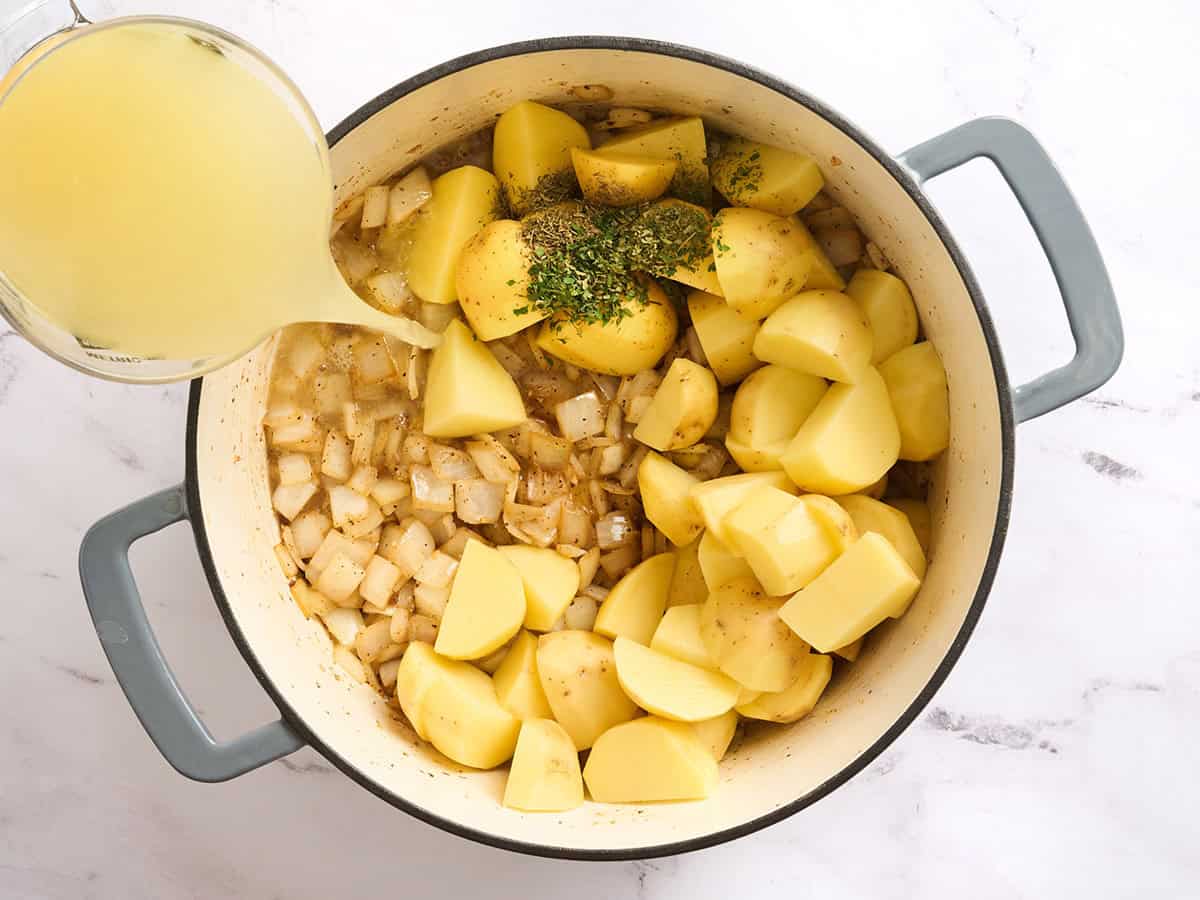 Broth being poured on top of vegetables in a dutch oven.
