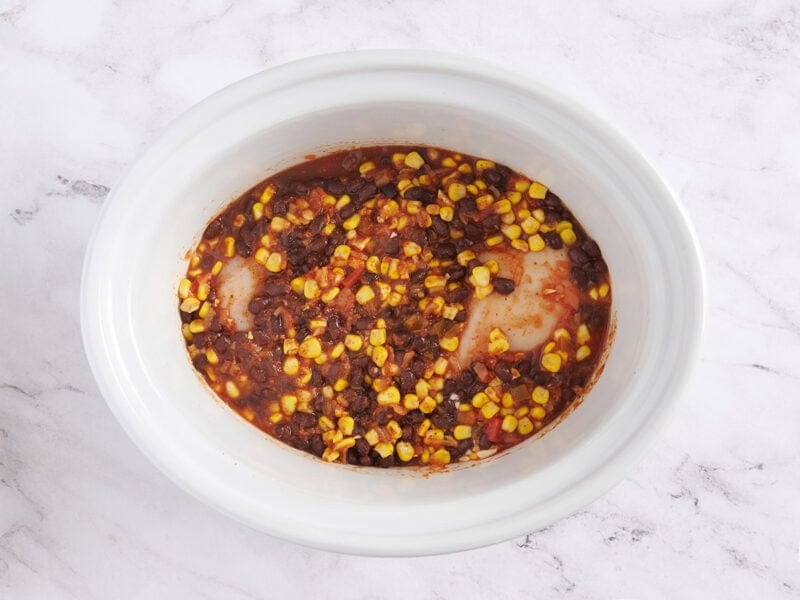 Combining the ingredients for taco chicken bowls in the crockpot.