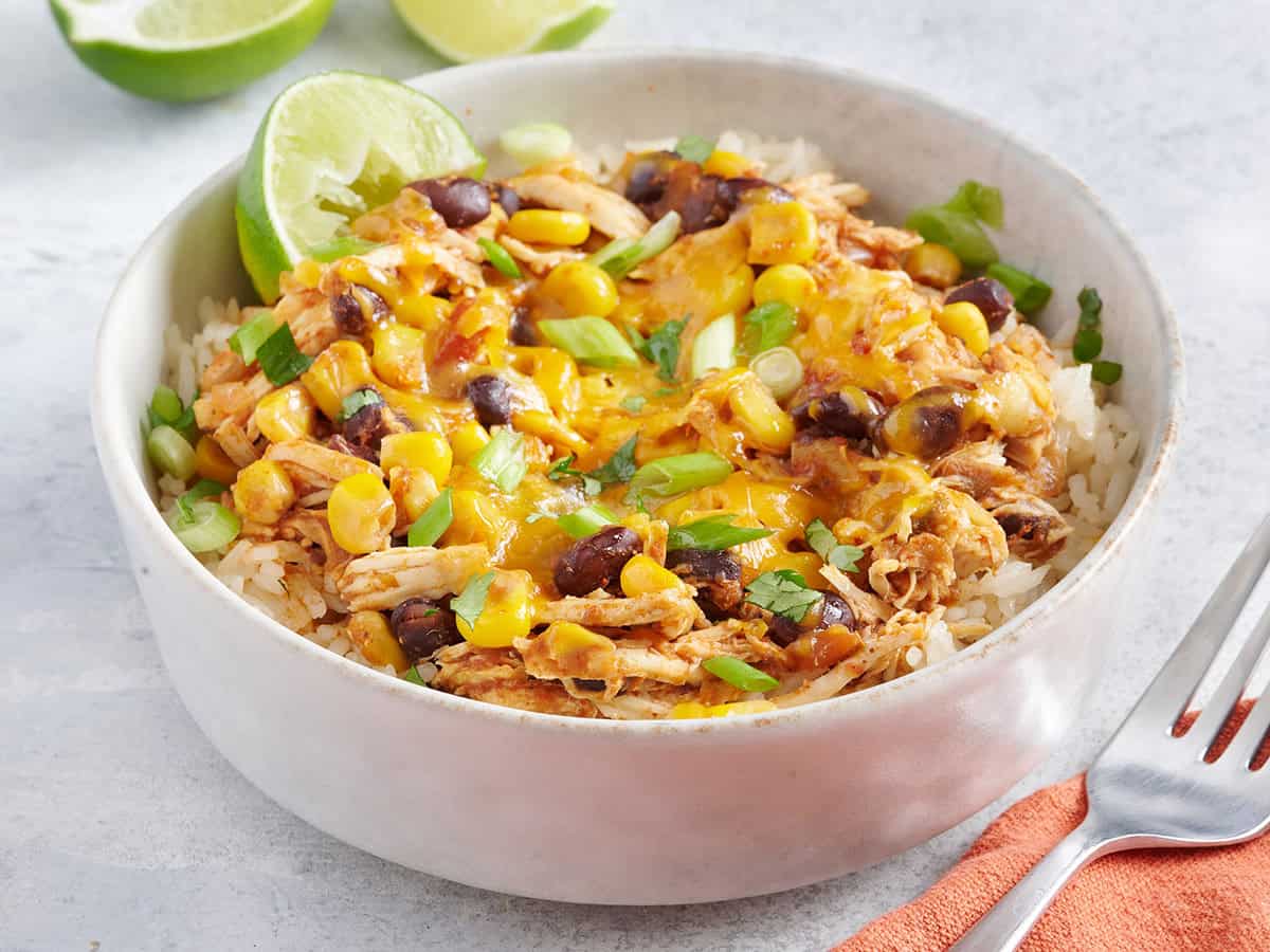 Slow Cooker Taco Chicken Bowls are the ultimate "set it and forget it" easy weeknight meal that the whole family will love. BudgetBytes.com Bowl of white rice with slow cooker chicken tacos.