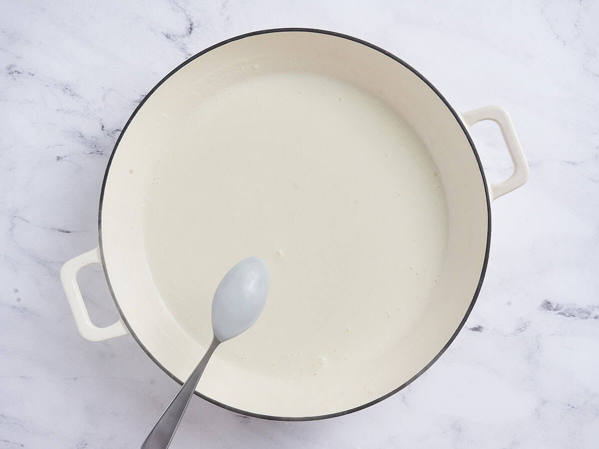 A spoon checking the thickness of a creamy sauce for mac and cheese.