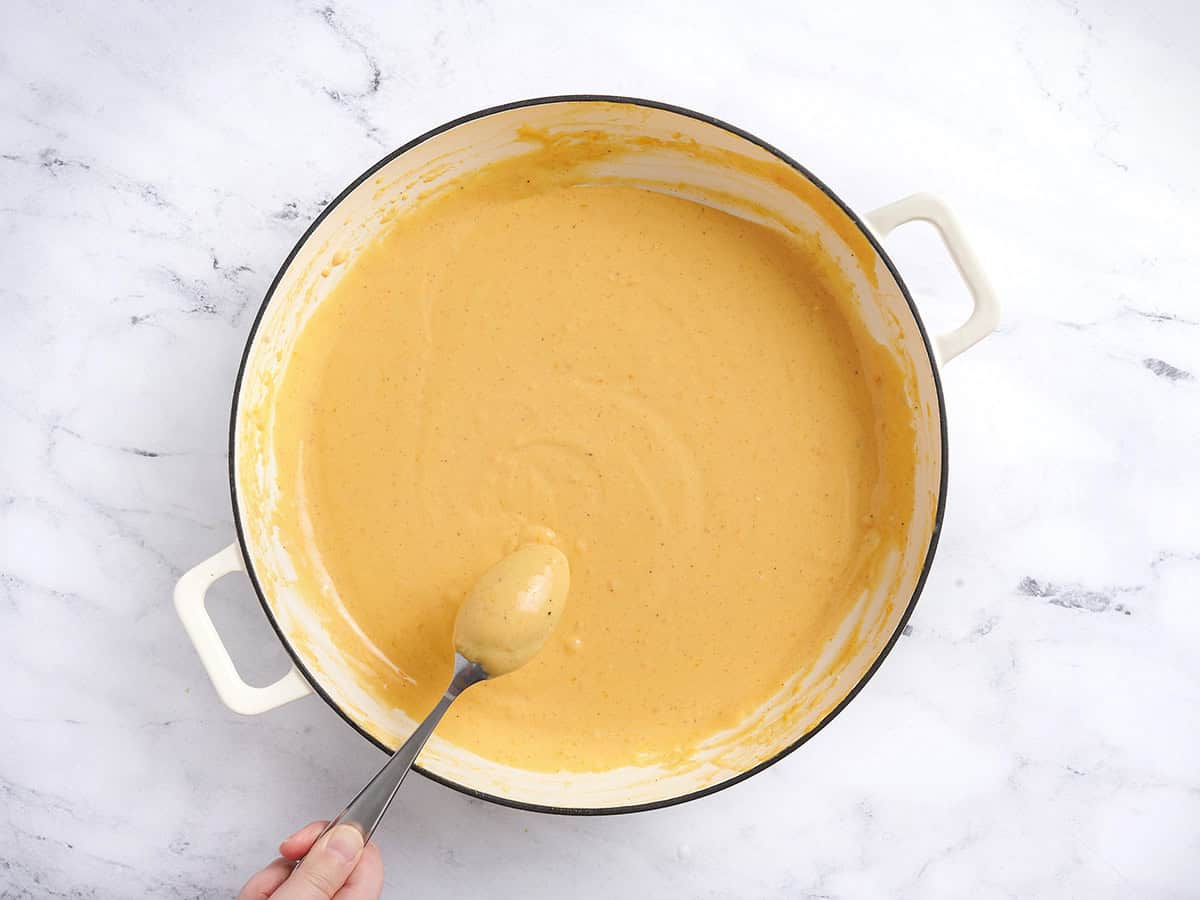 A spoon checking the thickness of a cheese sauce for mac and cheese.