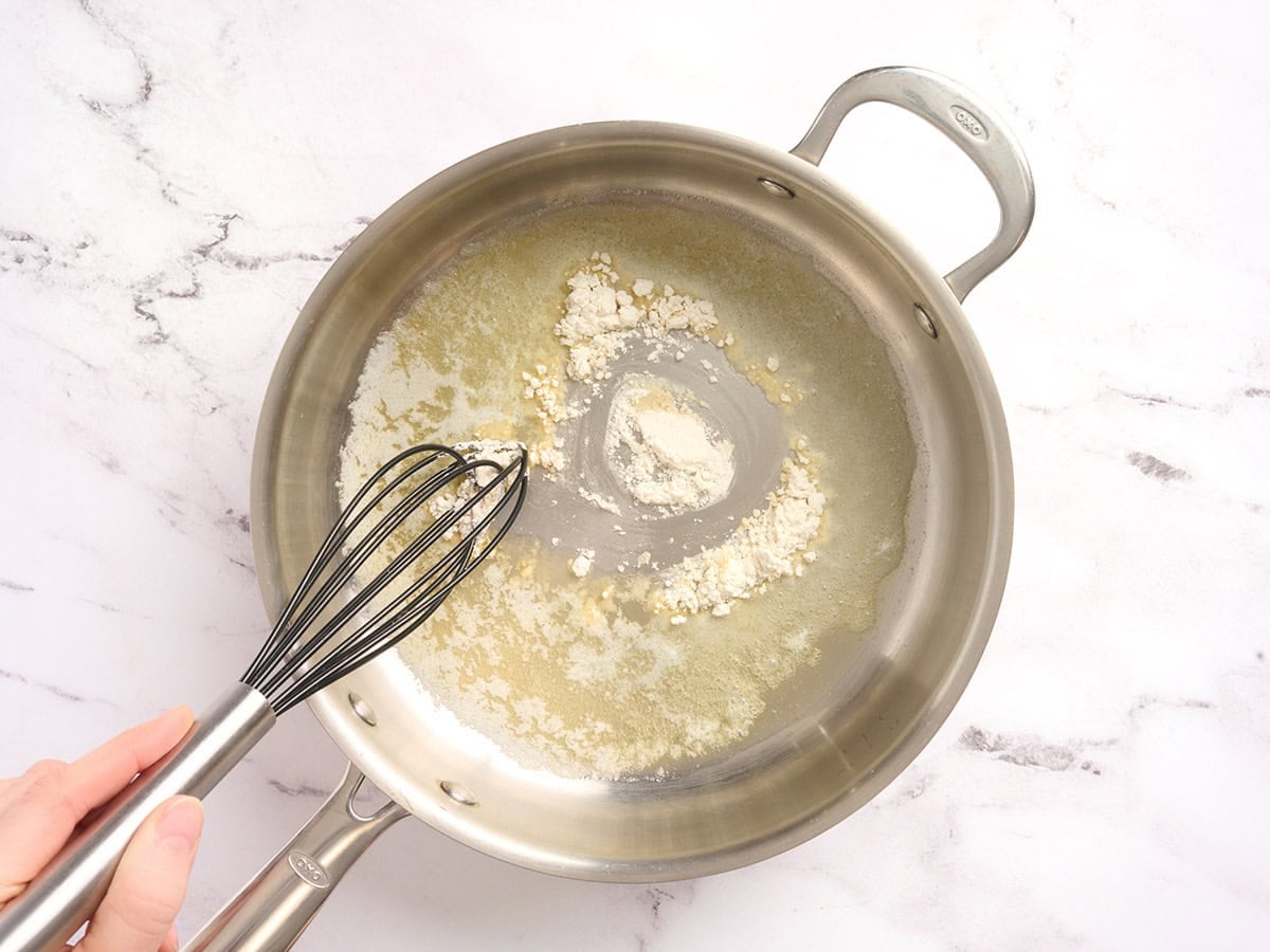 A whisk mixing a roux in a skillet.