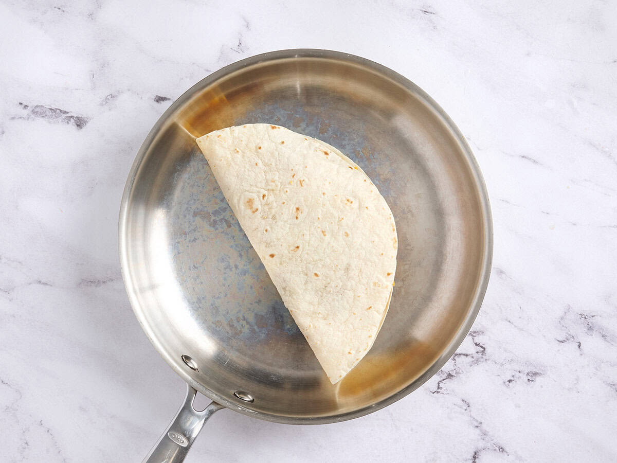 A folded tortilla cooking in a skillet.