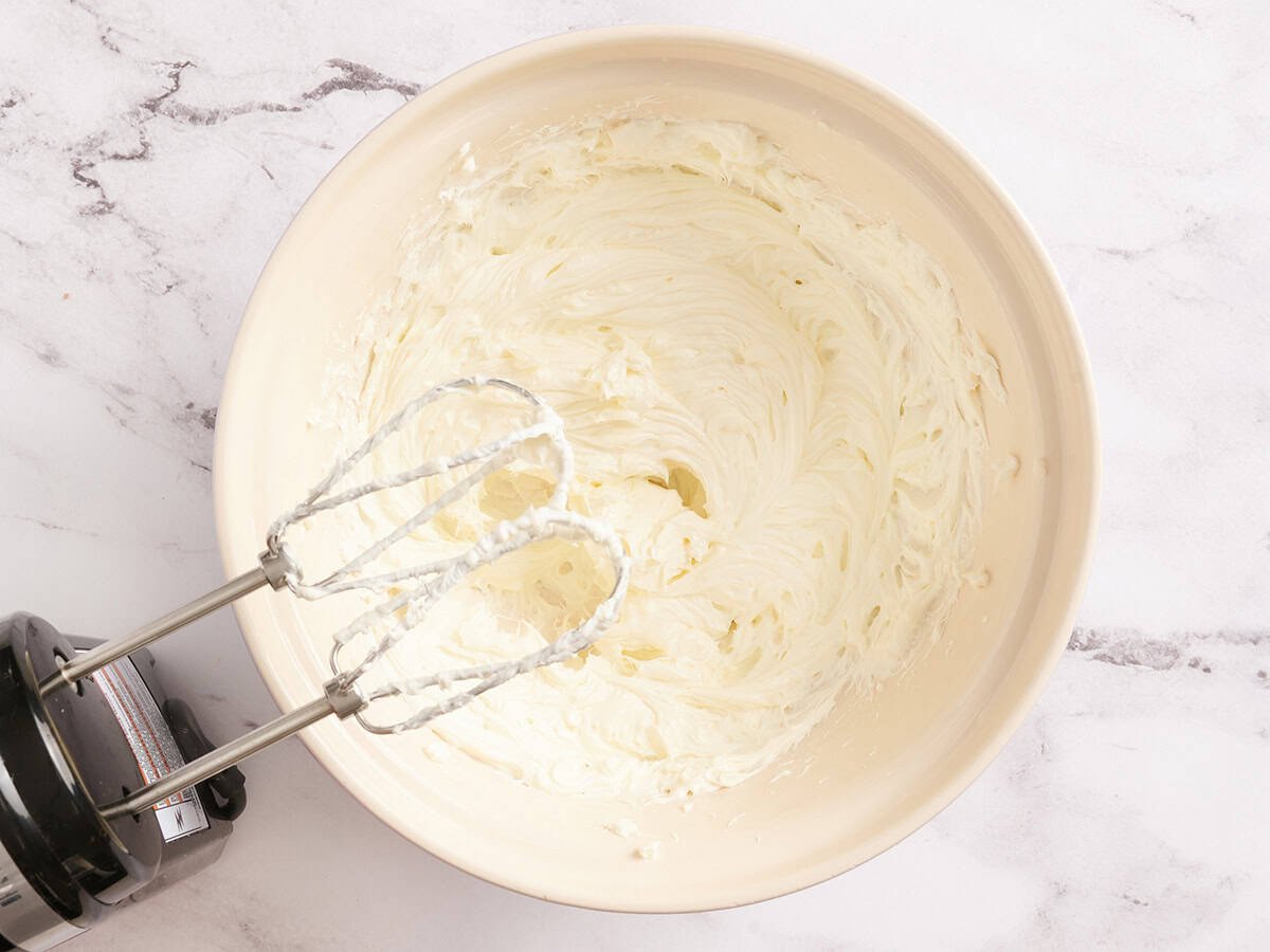 Beaten cream cheese in a bowl with a hand mixer.