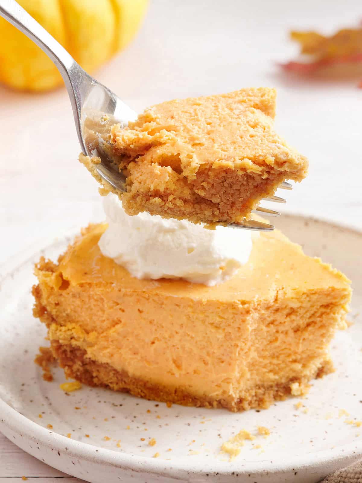 Sideview of a slice of pumpkin cheesecake on a plate with a fork taking some.