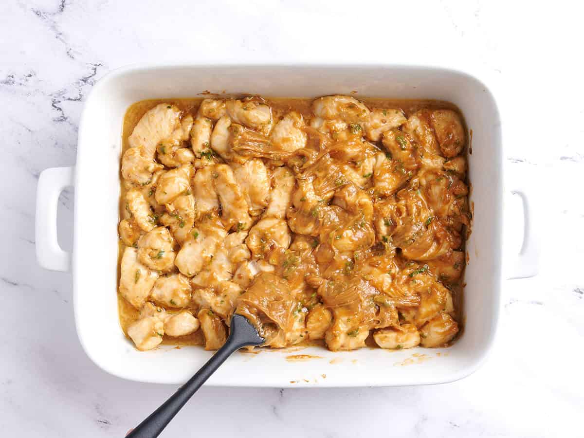 Peanut sauce added to chicken pieces in a baking dish.
