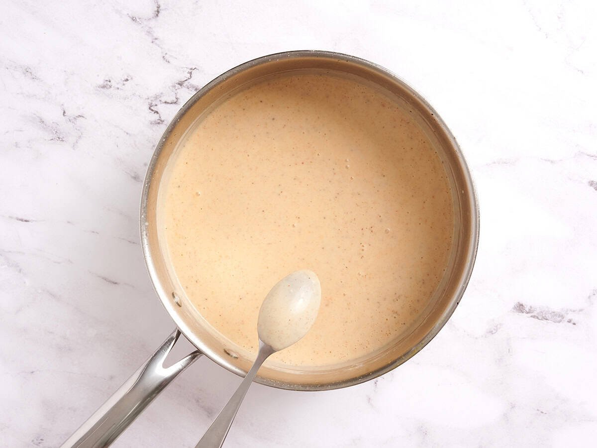A spoon checking the thickness of a creamy sauce for chicken and rice casserole