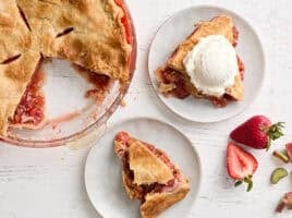 Overhead view of two slices of strawberry rhubarb pie on two plates, with one topped with ice cream.