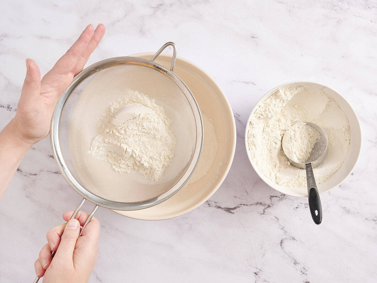 A hand sifting flour into a bowl.