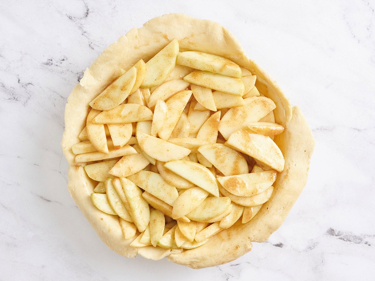 Apple slices in a pie dish lined with a pie crust.