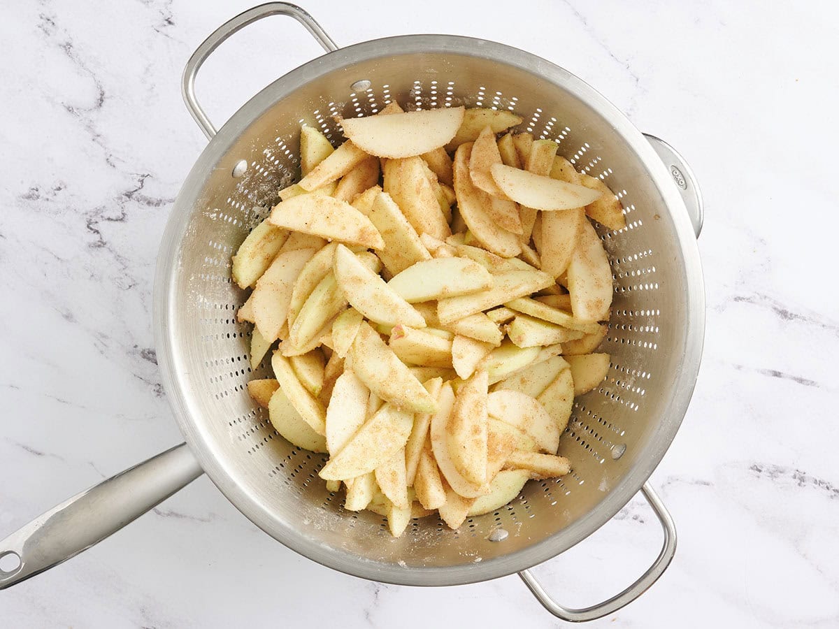 Apple slices tossed with cinnamon and sugar in a colander.