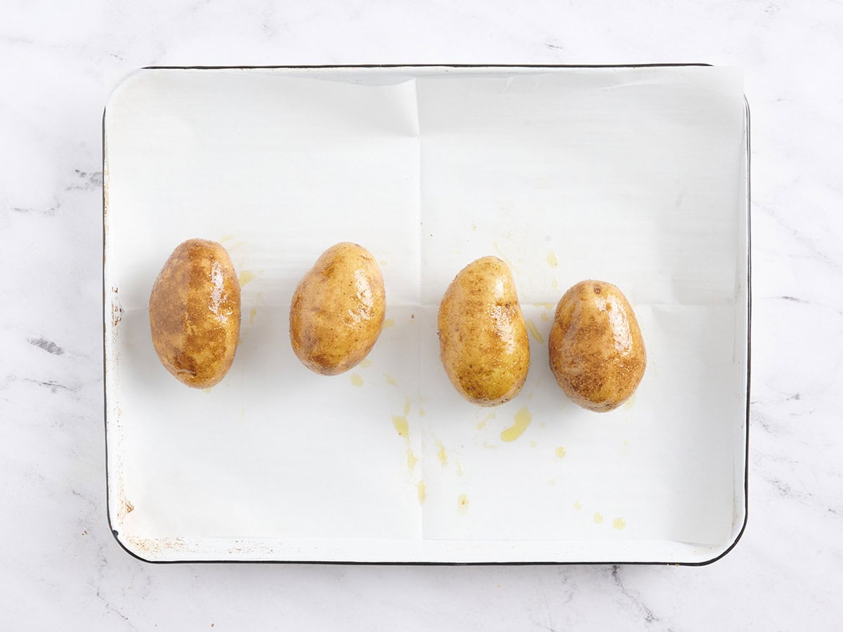 Four potatoes on a baking sheet with oil and seasonings
