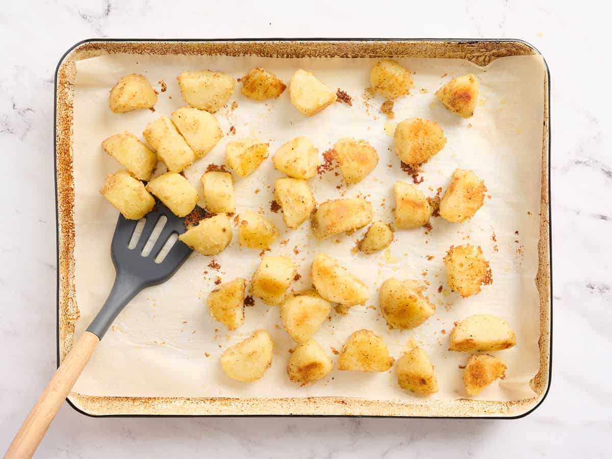A spatula flipping roasted potatoes on a baking sheet.