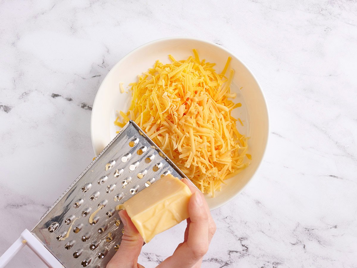 A hand using a grater to shred cheese.