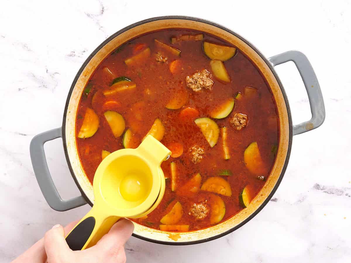 Half a fresh lime being squeezed into a pot of Mexican meatball soup.