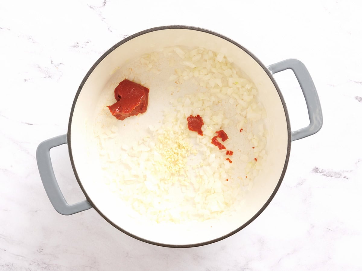 Tomato paste and minced garlic added to sauteed onion in a pot.