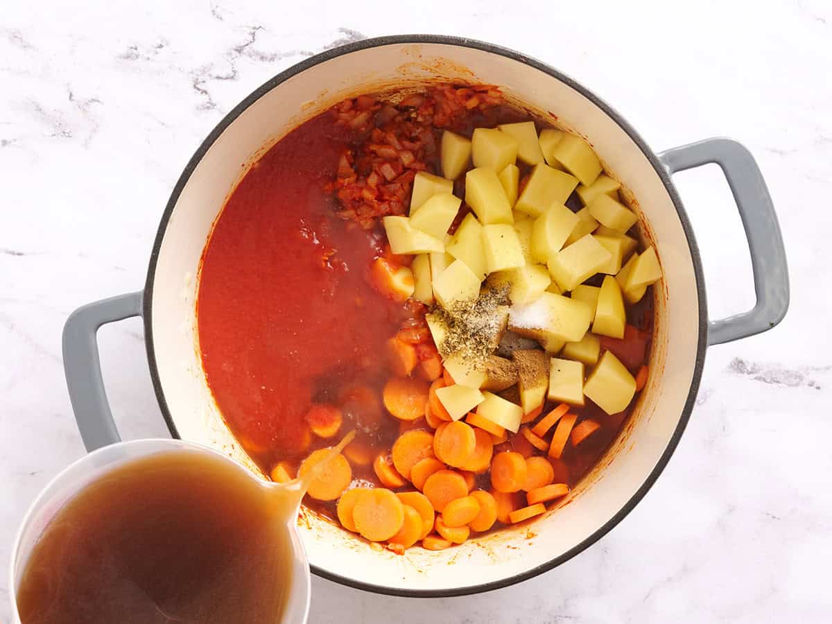 Broth, tomato sauce, vegetables, and spices in a pot.
