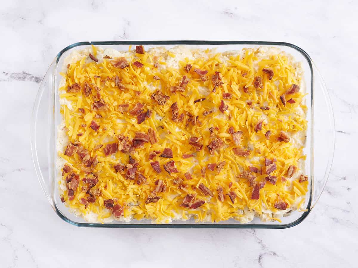 The filling for a twice baked potato casserole topped with shredded cheese and crumbled bacon pieces.