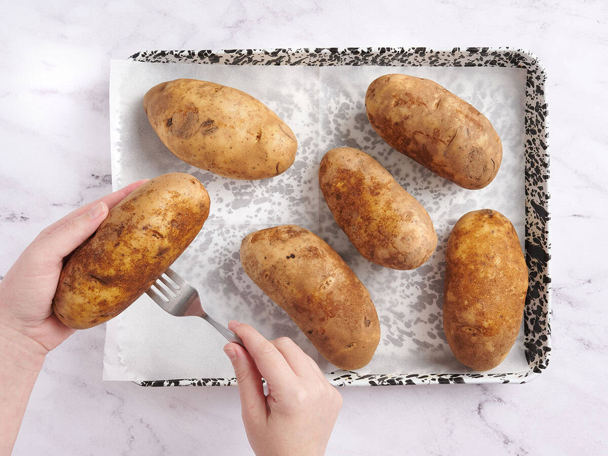 Hands using a fork to prick potatoes before baking.