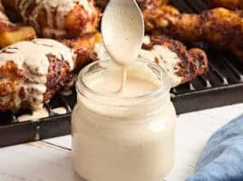 Homemade alabama white sauce in a glass mason jar with a spoon being pulled out covered in sauce.