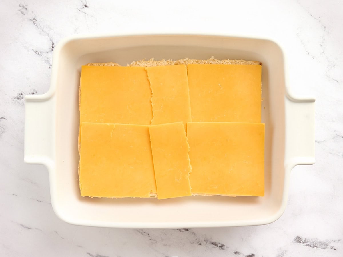 A layer of american cheese on top of sliced Hawaiian sliders.