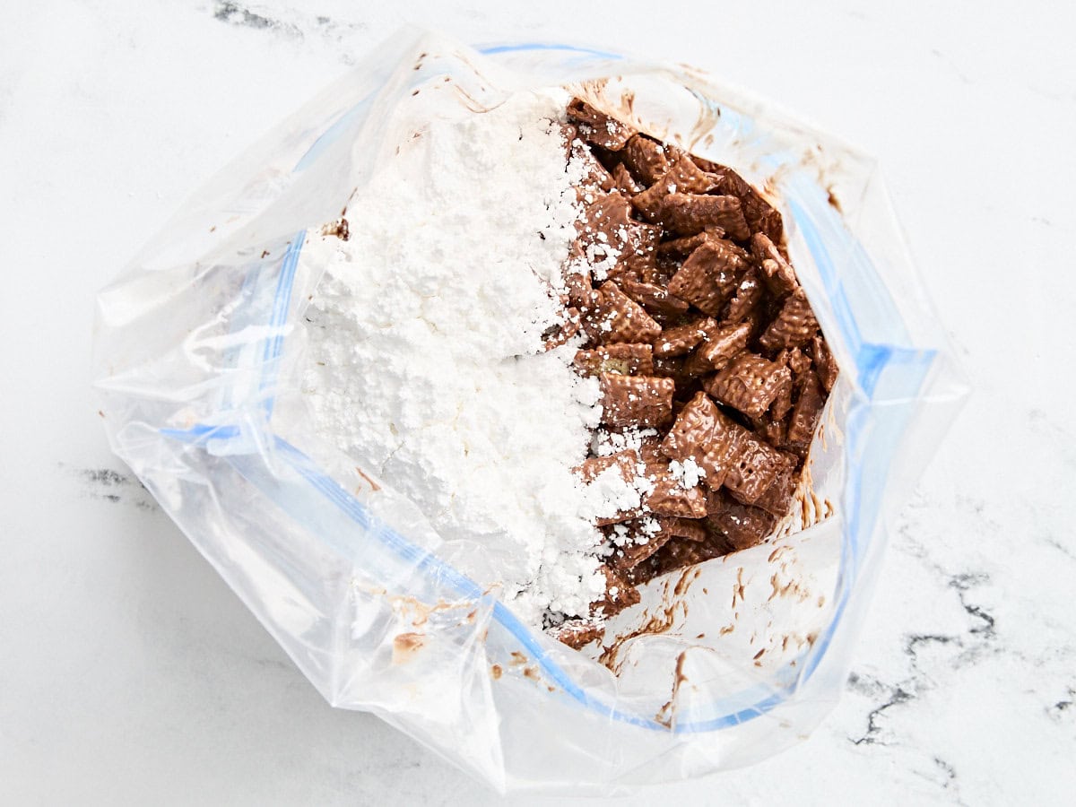 Chocolate covered rice chex cereal in a bag with powdered sugar.