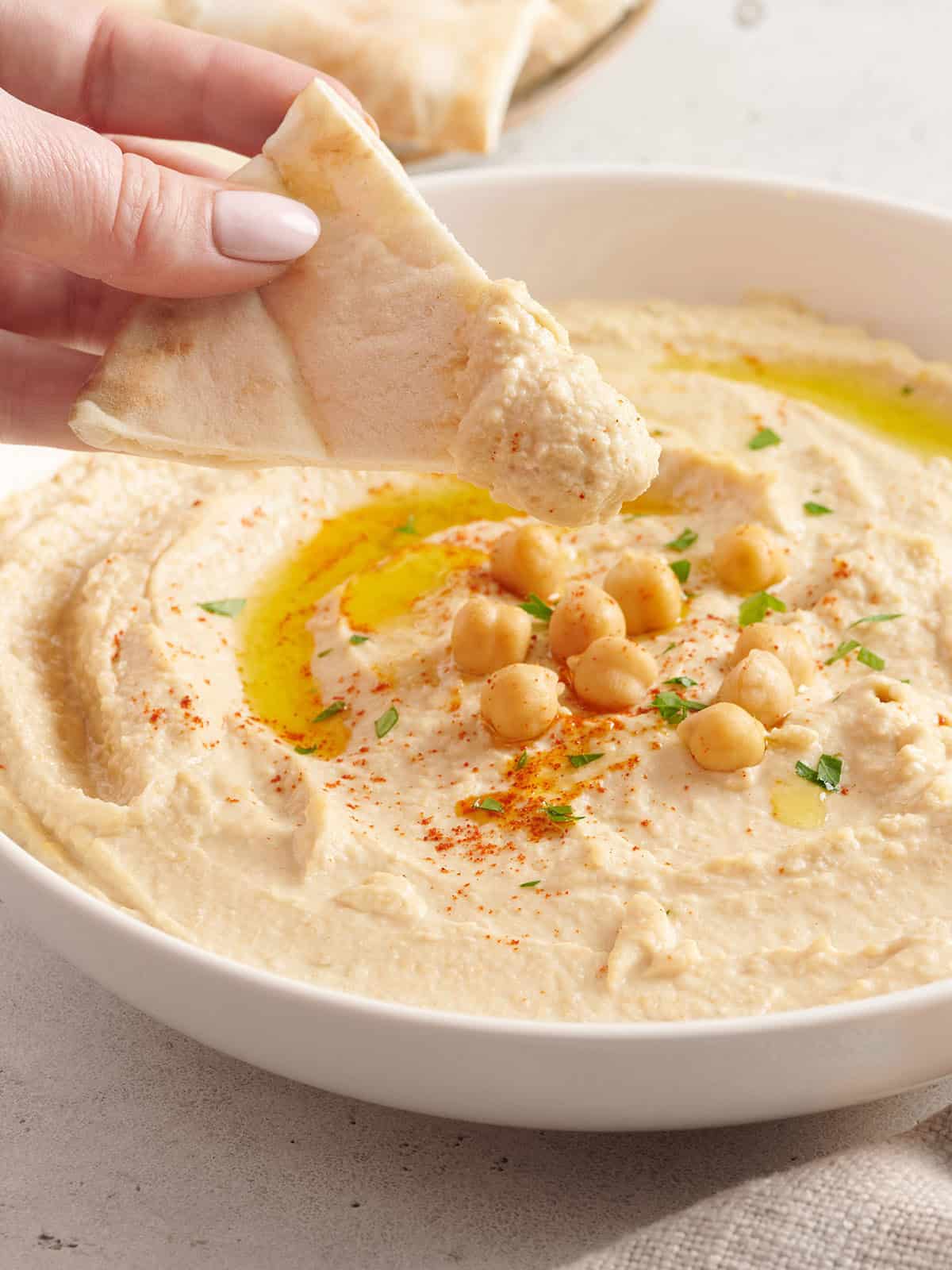 Side view of a hand holding a chip after being dipped in hummus.