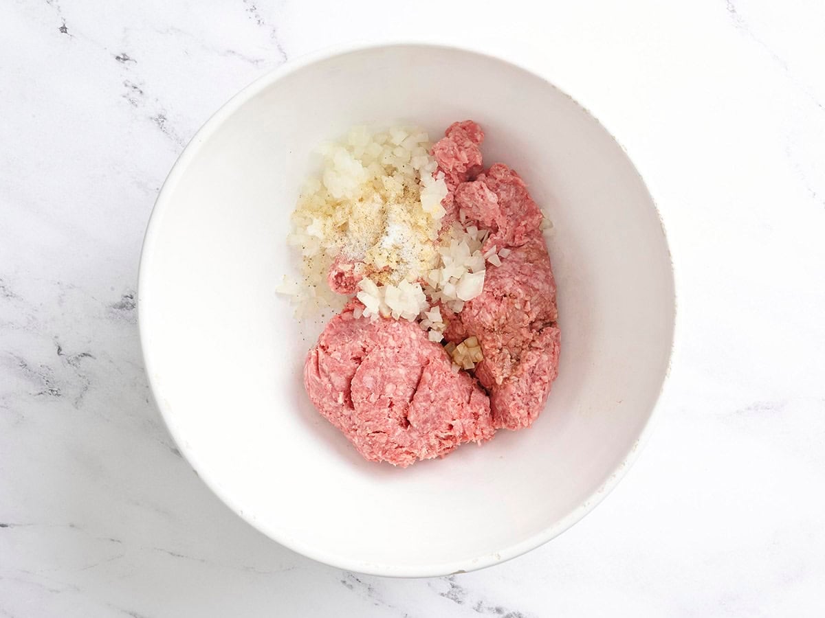 Ground beef, minced onion, and seasoning in a mixing bowl.
