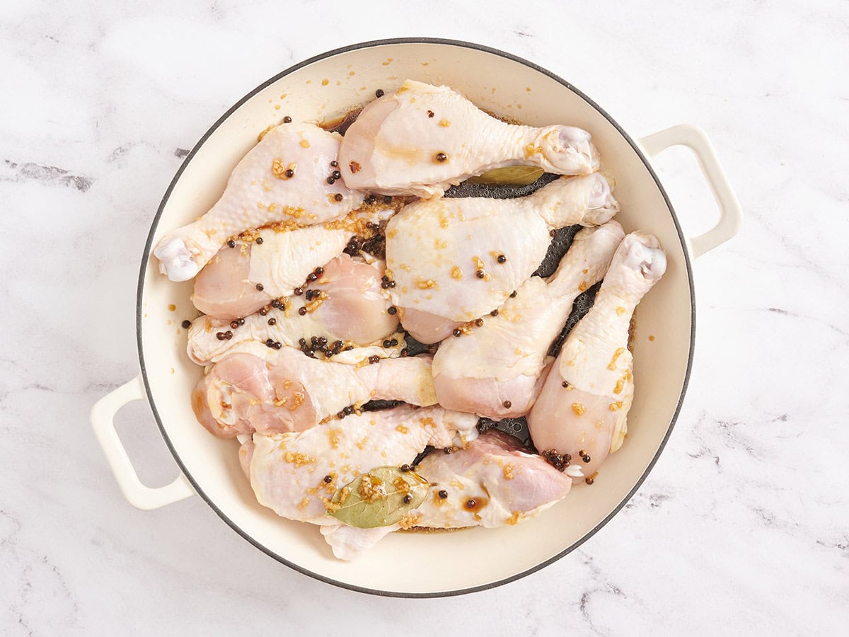 Chicken drumsticks covered in a marinade in a pot.