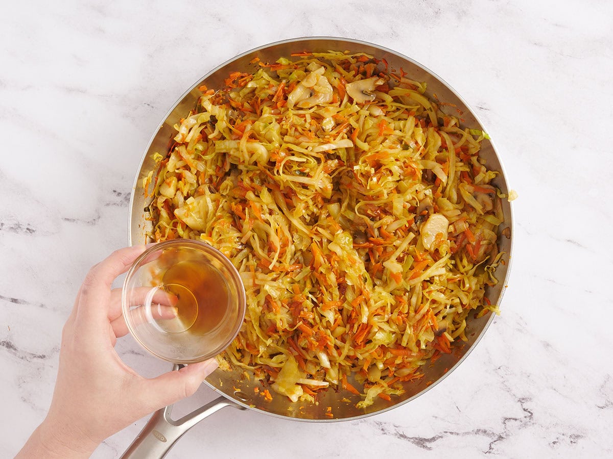 Sesame oil being poured into a skillet of sauteed vegetables.
