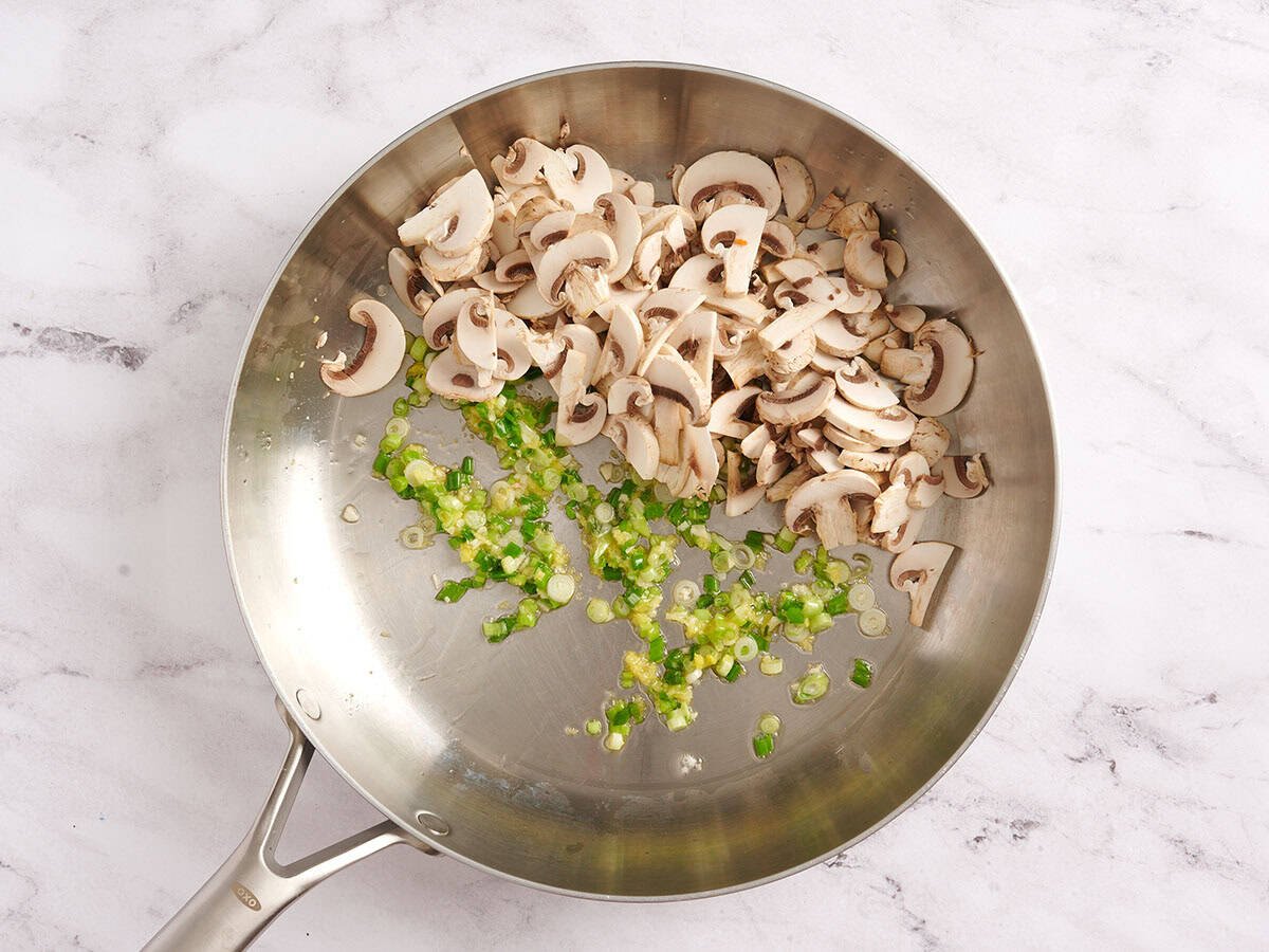 Mushrooms in a skillet with sauteed green onions.