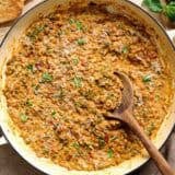 Overhead view of marry me lentils in a skillet with a wooden spoon.