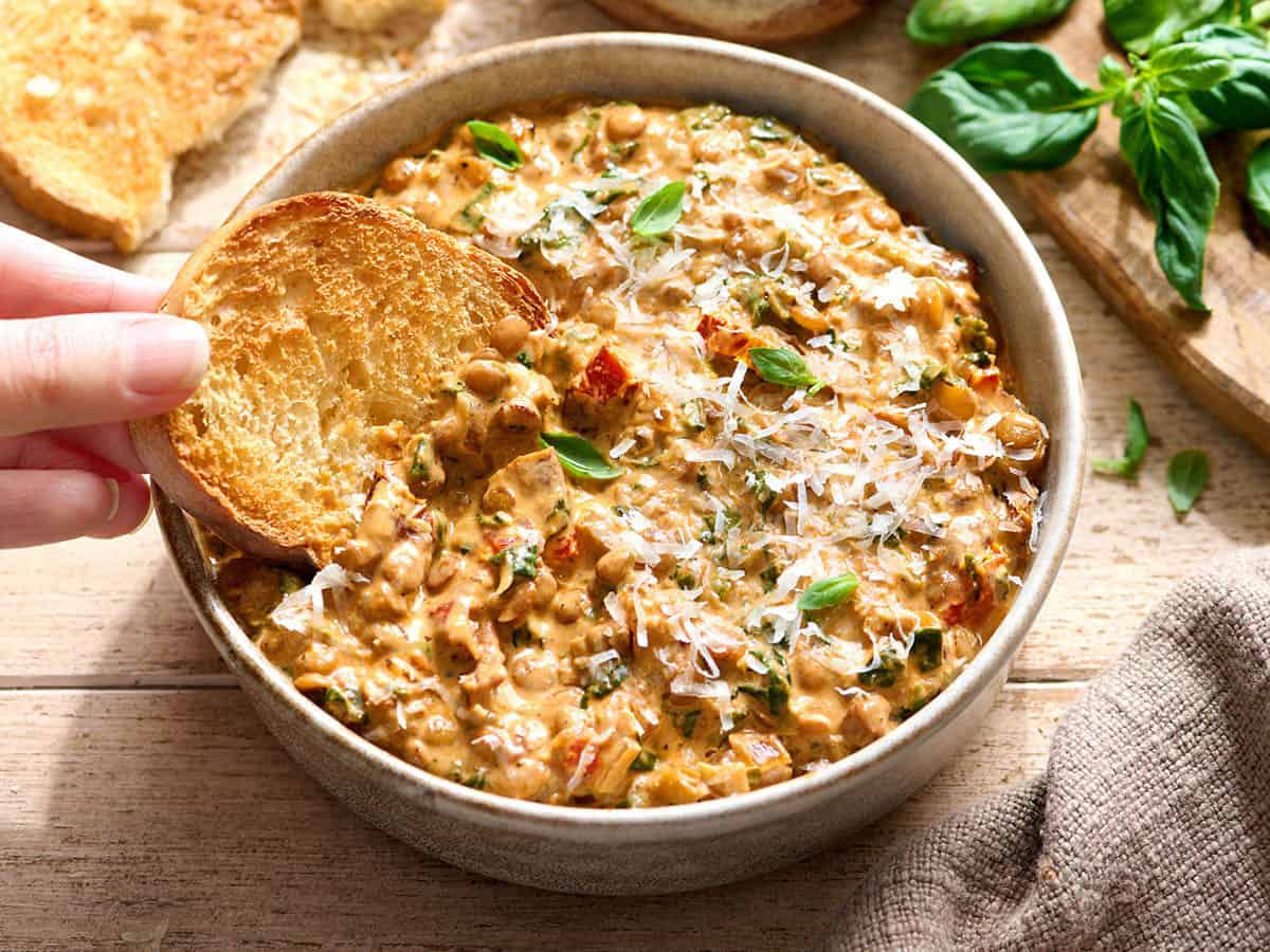 A hand dipping a slice of toasted bread in a bowl of marry me lentils.