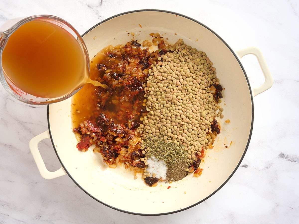 Broth and dried lentils added to a pot with sundried tomatoes.