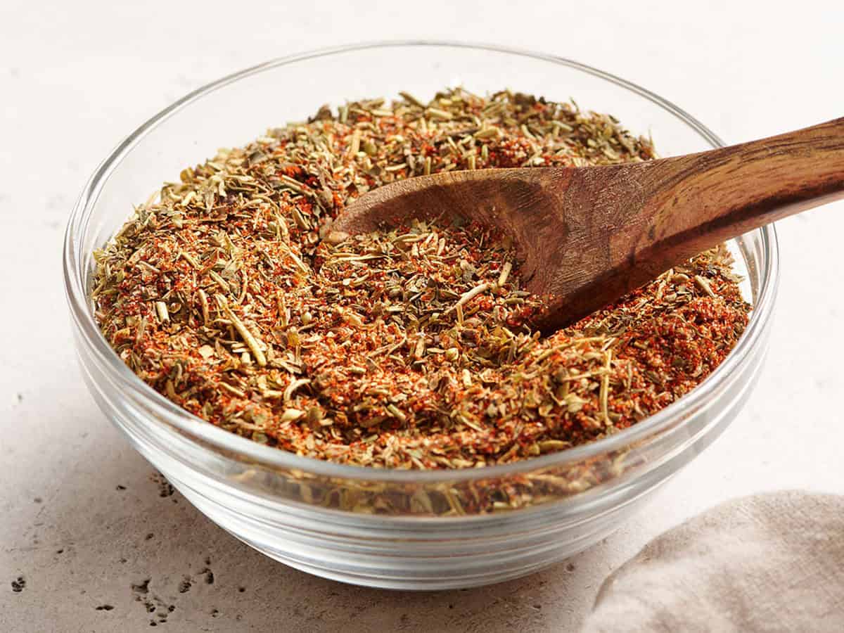 Side view of a bowl of poultry seasoning with a wooden spoon.