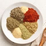 The individual spices and herbs for homemade poultry seasoning on a plate.