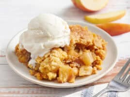 Side view of apple dump cake on a plate with a scoop of vanilla ice cream.