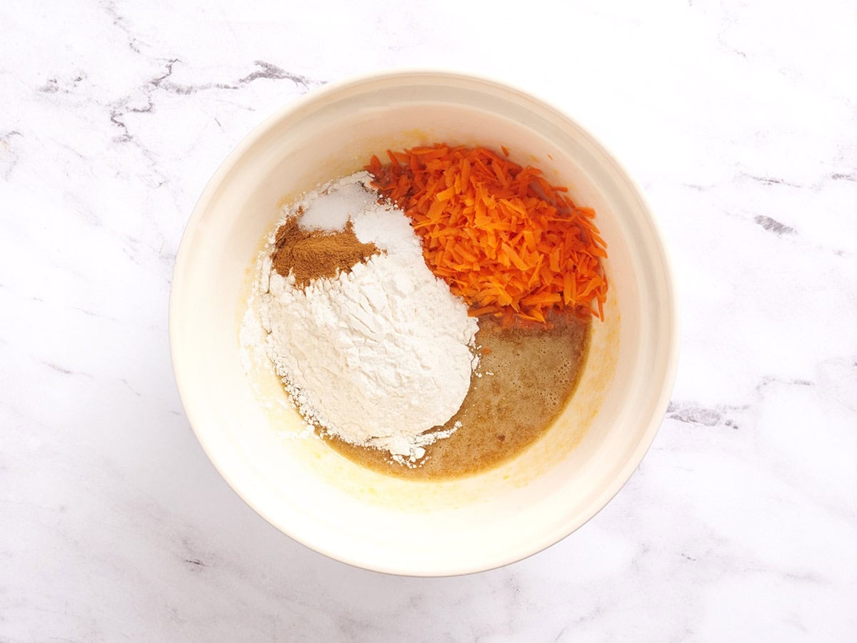 Flour, spices, grated carrots and cake batter in a bowl.