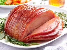 Side view of sliced honey glazed ham on a plate with herbs.