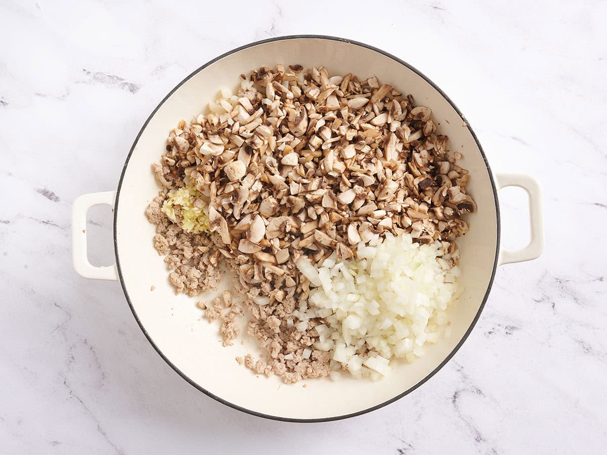 Adding onion, garlic, ginger, and mushrooms to the skillet with the cooked turkey.