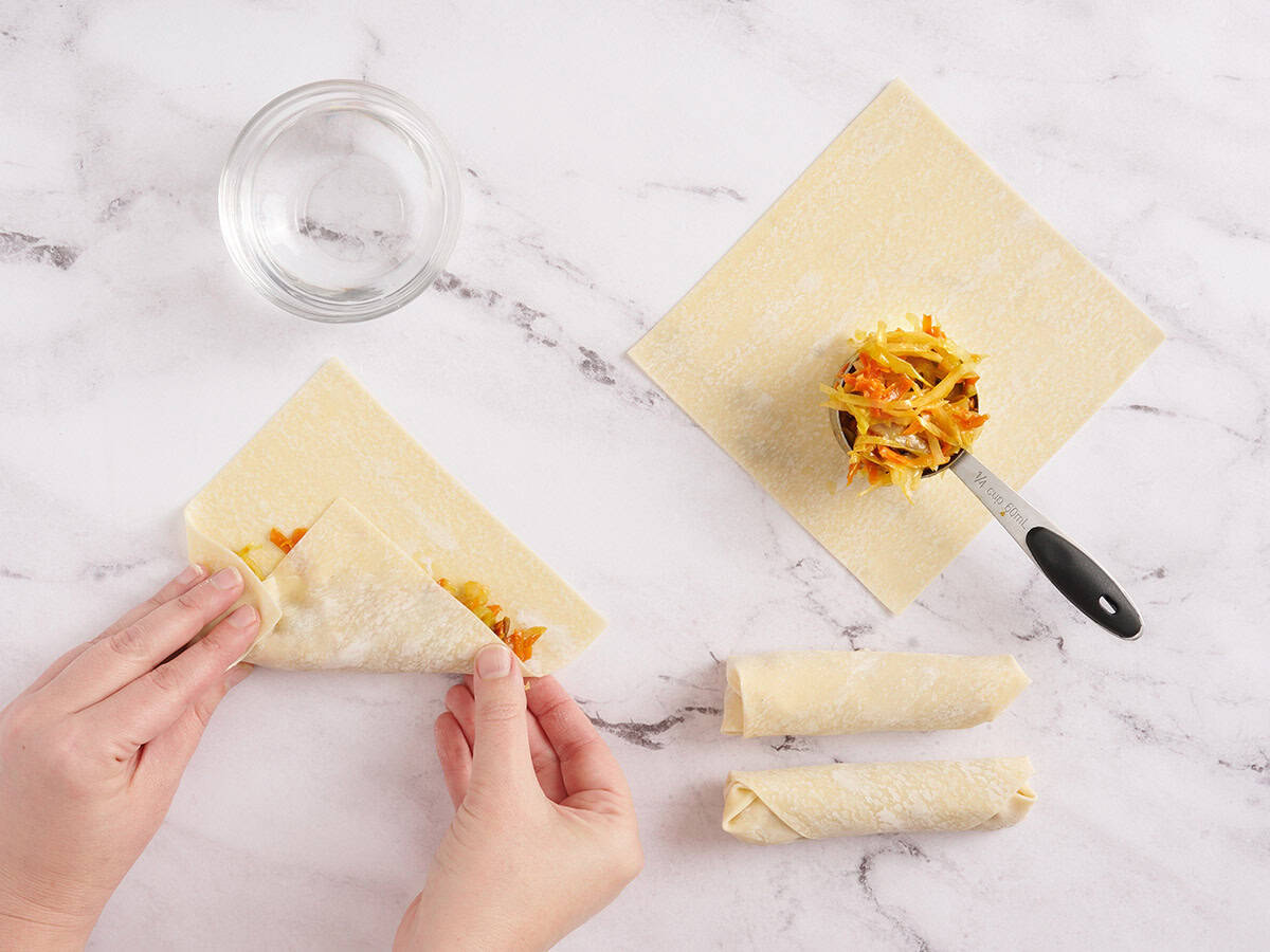 A hand rolling vegetable egg rolls.