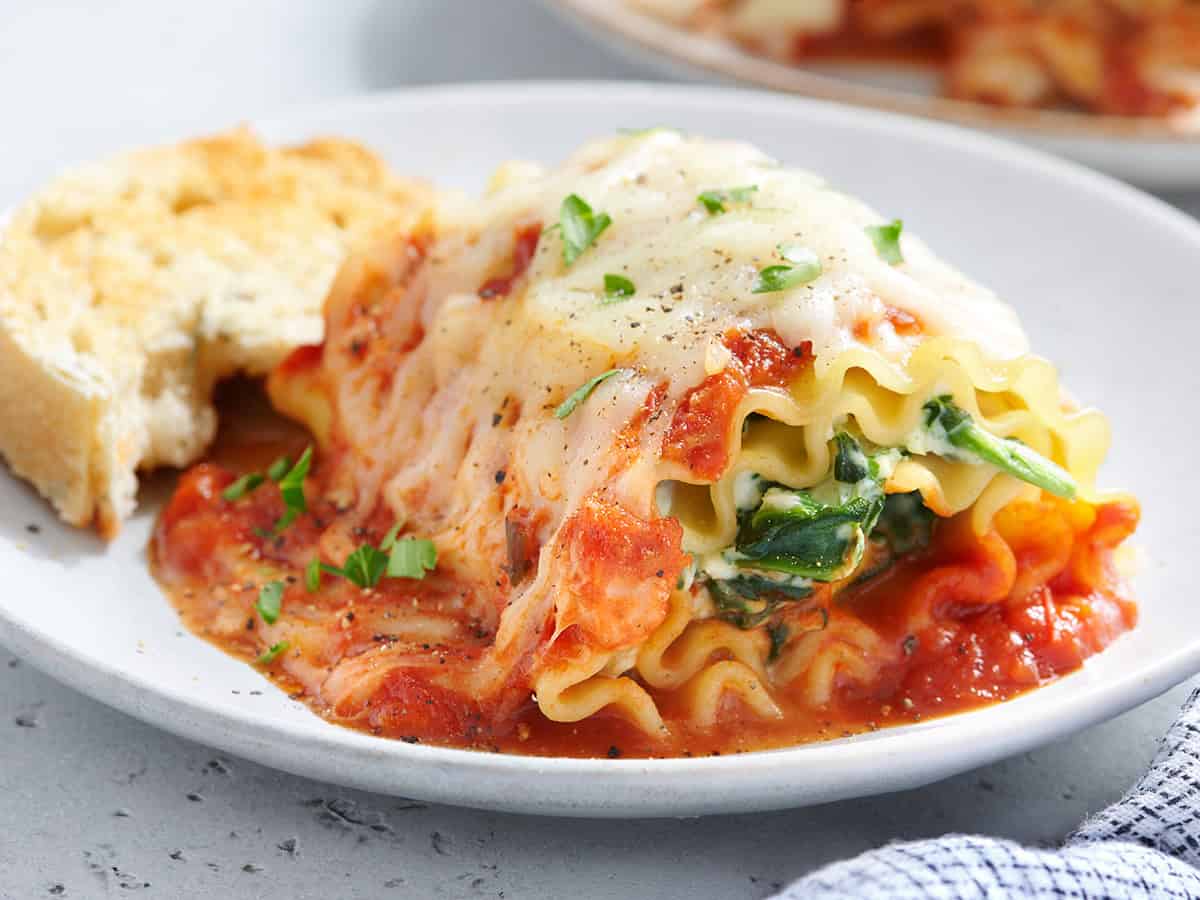 Side view of a spinach and ricotta lasagna roll up on a plate with bread.